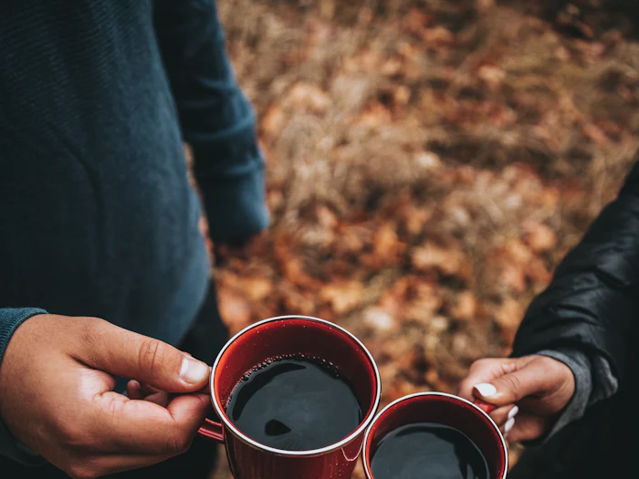 Three mugs of coffee raised over autumn leaves